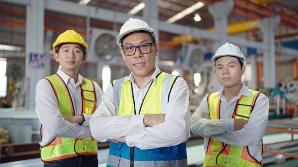 equipe de retratos de engenheiros asiáticos homens em uniforme de segurança olhando para a câmera enquanto estão de braços cruzados na fábrica industrial. conceito de trabalho em equipe - manager foreman warehouse arms crossed - fotografias e filmes do acervo