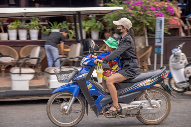 Luang Prabang, Laos - March 11th 2023: Mother and child driving down the street on a motorcycle