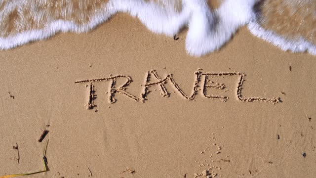 Text TRAVEL handwritten in sand surface. Blue ocean wave washing away message at the beach. Summer holidays writing concept