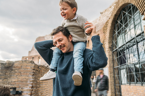 Child flying on father shoulders while held piggyback