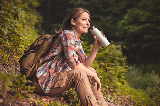 Female Hiker Drinking Water From Water Bottle or Hot Drink From Thermos Surrounded by Nature During Holiday Vacation Trip