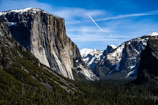 A scenic view of a snowy mountain range covered green forests in Yosemite Park, California