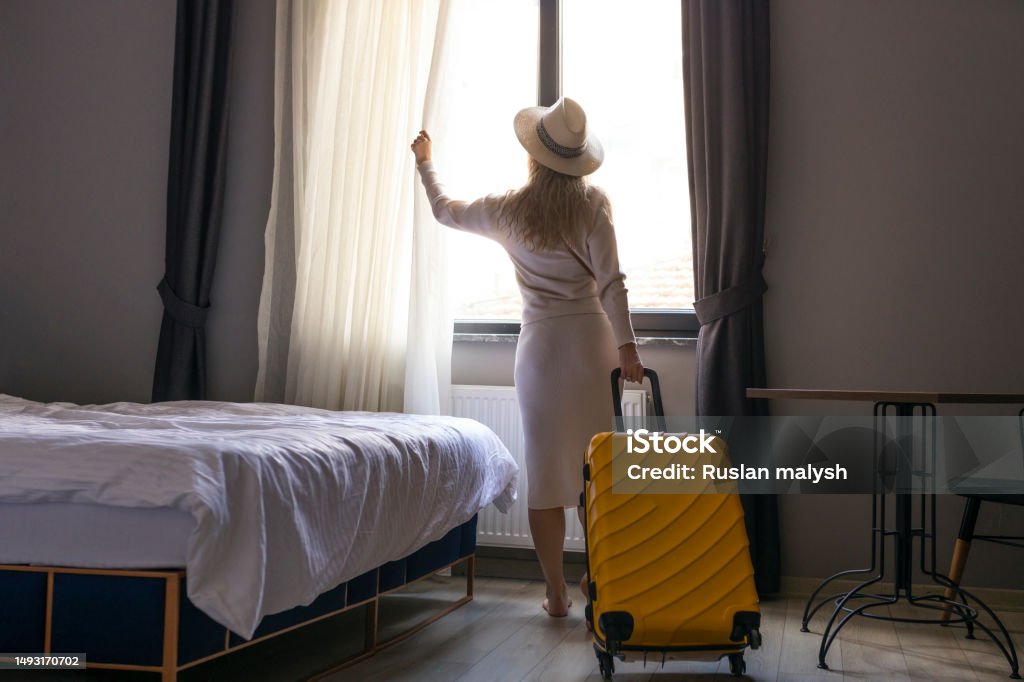 Portrait of tourist woman standing nearly window, looking to beautiful view with her luggage in hotel bedroom after check-in. 30-34 Years Stock Photo