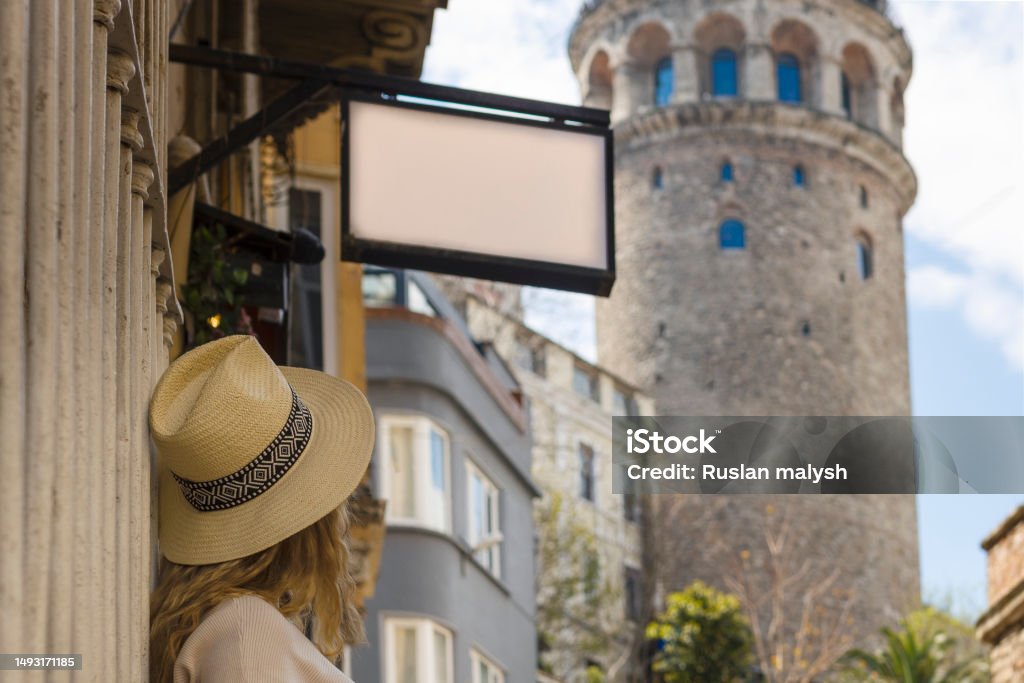 A girl in a hat looks at the Galata tower, and above it hangs a mockup with an empty space for the logo A girl in a hat looks at the Galata tower, and above it hangs a mockup with an empty space for the logo. 30-34 Years Stock Photo