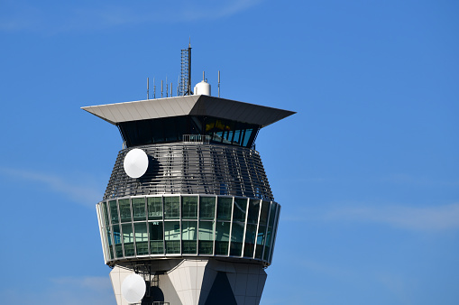 Airport traffic control tower on summer day with blue sky behind. Communication lookout tower communication with jet planes taking passengers on holiday. Copy space to the right.