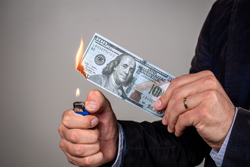 Person burning a hundred dollar bill. Burning hundred dollar bill. Man setting fire to US banknote.