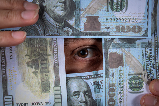 Human eye through the hundred dollar bills. Eye of a person surrounded by hundred dollar bills. Several hundred dollar bills. Person looking through hundred dollar bills