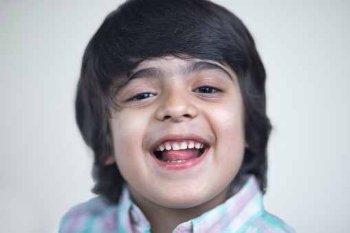 Image of little Indian cheerful boy posing towards the camera - white background, wearing casuals