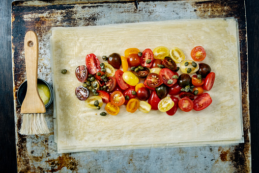 Burrata served with roasted tomatoes with filo pastry. Colour, horizontal format with some copy space.
Take 8 sheets of filo pastry, brushing with melted butter in-between each layer, on top of the last layer place some sliced cherry tomatoes, season with salt and pepper and add the capers, leave enough room around the edge to fold the edges over to make a “parcel”. Bake for 20 minutes until the filo pastry turns a rich golden brown colour, allow to cool on a wire tray then cut serve with fresh burrata and basil leaves. Delicious!