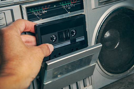 A woman's hand inserting a cassette tape into a boom box stereo.