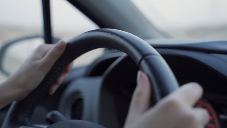 Close up of young woman's hands on vehicle steering wheel as she is driving