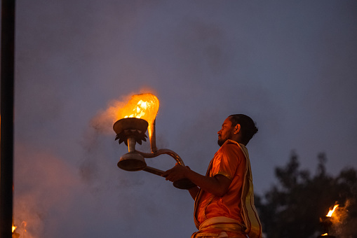 Varanasi, Uttar Pradesh, India - November 2022: Ganga aarti, Portrait of an young priest performing river ganges early morning aarti at assi ghat in traditional dress with fire flame traditionally.