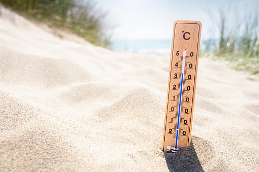 Thermometer in sand on the beach reading high temperature in the summer sun background