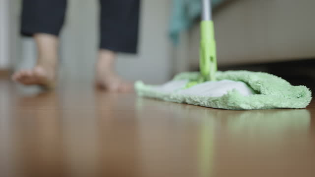Unrecognizable woman holding green mop and mopping from left to right