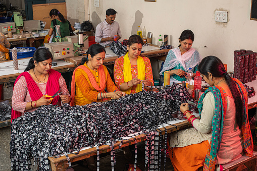 Female workers cutting printed garments on table at textile factory and representing women empowerment