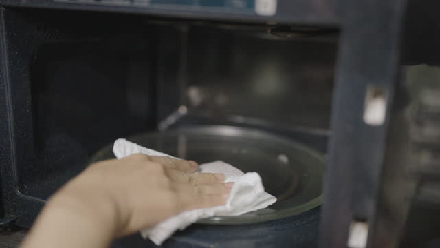 Unrecognizable woman cleaning the insides of black microwave