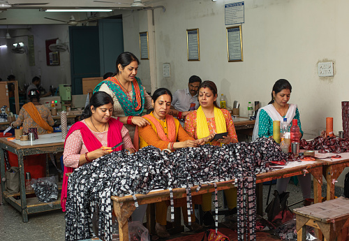 Female workers cutting printed garments on table at textile factory and representing women empowerment