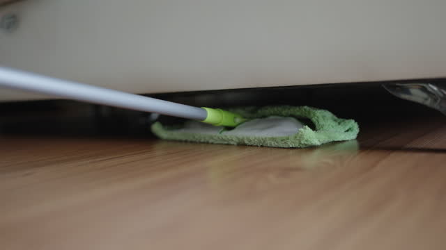 Unrecognizable using green mop to clean under bed
