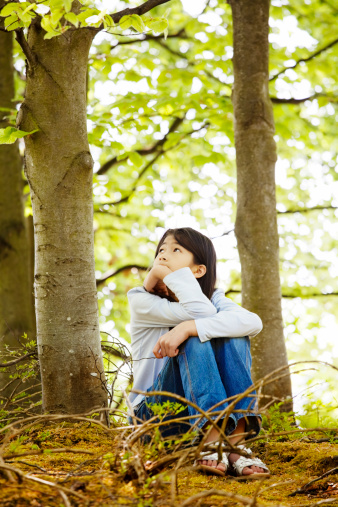 Ten year old girl sitting quietly in woods, looking around thinking