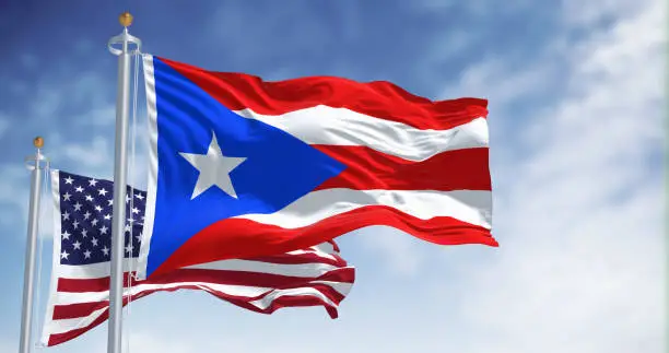 Flag of Puerto Rico waving with the United States flag on a clear day. Puerto Rico is a Caribbean island and unincorporated territory of the United States. 3D illustration render. Fluttering fabric
