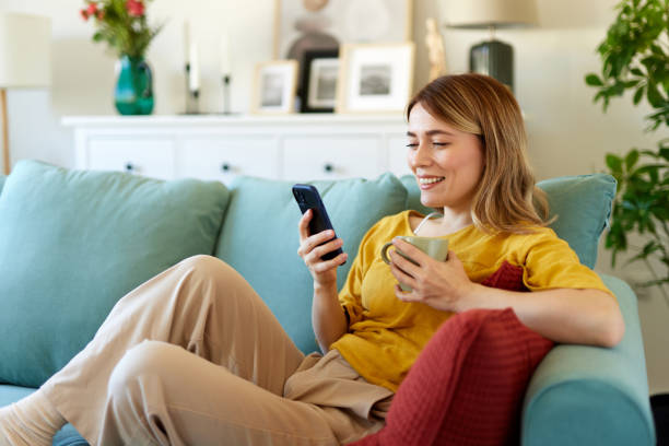 Woman using smartphone while drinking coffee at her home in the morning