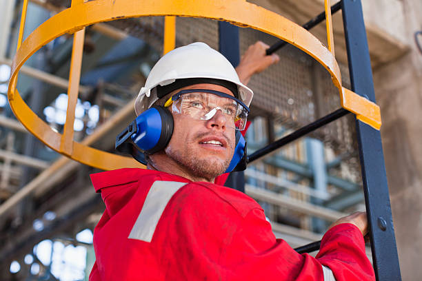 pracownik wspinaczka drabiny na rafineria naftowa - construction safety protective workwear hardhat zdjęcia i obrazy z banku zdjęć