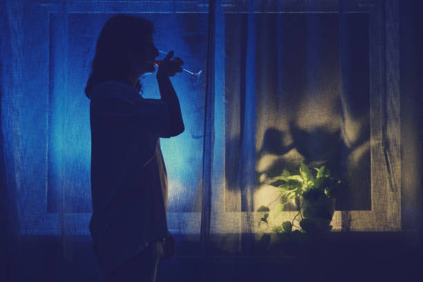une femme boit du vin dans un verre à la fenêtre sombre de la nuit, silhouette discrète. problèmes d’alcoolisme féminin et de solitude - eastern european caucasian one person alcoholism photos et images de collection