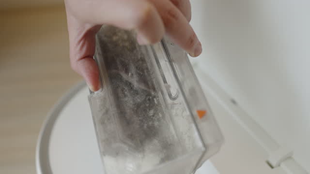 Opening automated vacuum cleaner revealing dust filled inside compartment