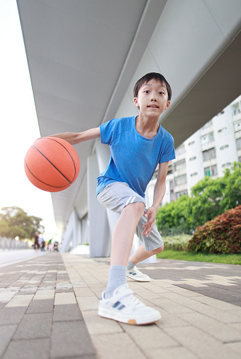 Cute male child in sportswear jumping in the air and holding basketball ball