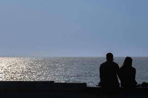 Back view of a couple silhouette hugging and watching horizon over the ocean on the beach