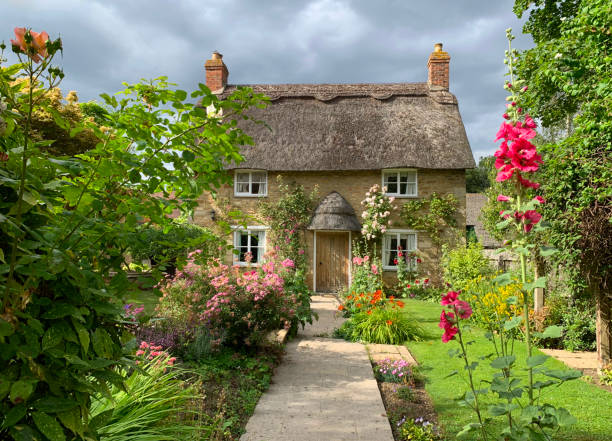 A gorgeous thatched cottage with a beautiful garden in a rural English village on a summer’s day. Rutland, UK - July 18, 2019: A charming thatched cottage with a beautiful garden in an English village. house uk countryside stock pictures, royalty-free photos & images