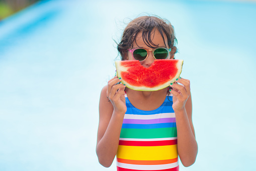 Child with watermelon in swimming pool. Summer sun and water fun. Healthy fruit snack for kids. Tropical fruits in family vacation. Travel with children. Little girl on beach holiday.