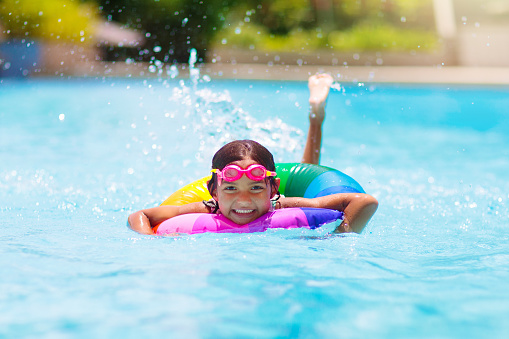 Child in swimming pool floating on toy ring. Kids swim. Colorful rainbow float for young kids. Little girl having fun on family summer vacation in tropical resort. Beach and water toys. Sun protection.