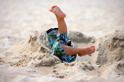 Child has fallen in a pit on the beach, only his legs are seen
