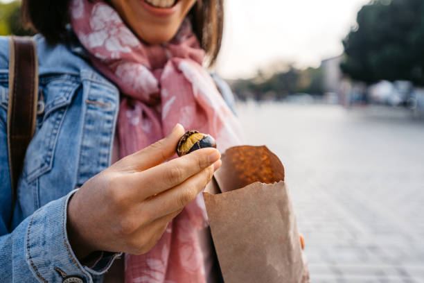mujer joven comiendo castañas asadas en la calle en estambul - chestnut roasted heat roasted chestnut fotografías e imágenes de stock