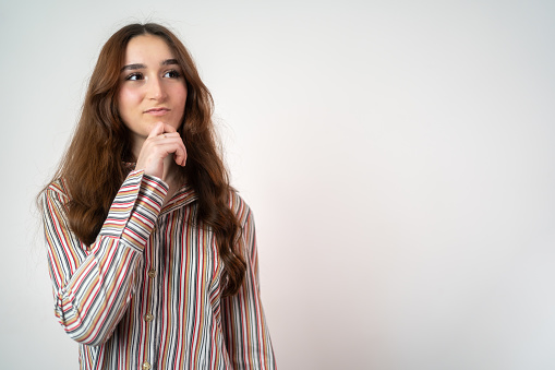 Front view of pensive pretty teenager girl. Long hair girl thinking on grey background. lady looking up empty space deep thinking creative person arm on chin wear casual shirt isolated white