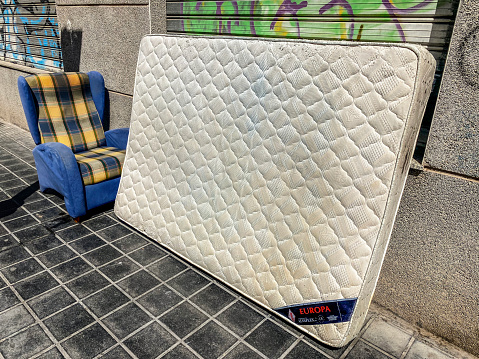 Valencia, Spain - May 21, 2023: Armchair and mattress left in the street. The city government has a service for gathering old objects that people throw upon request