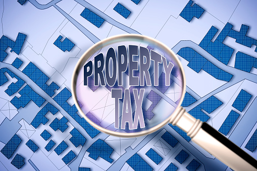 Property Tax concept image against an imaginary city map with a magnifying glass.