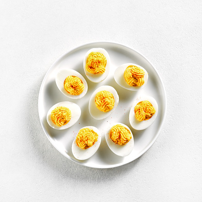 Deviled eggs with paprika, mustard and mayonnaise on plate over white stone background. Top view, flat lay