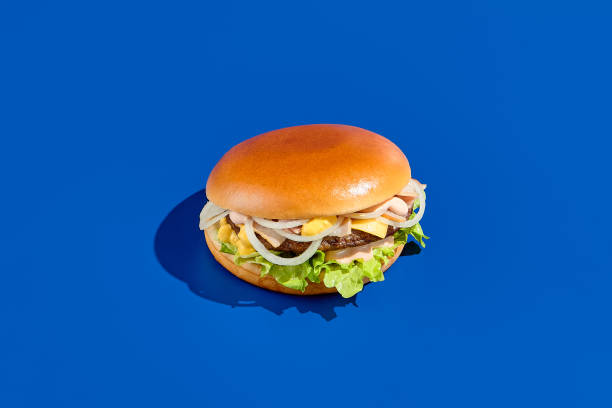 istock Delectable cheeseburger with onion, cheddar cheese, sauce on a blue background. A contemporary, minimalist food photography style perfect for to-go meals. Horizontal composition with space for text 1493258632