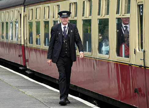 Grosmont, UK - August 16, 2021:   A guard walking along the platform by a vintage railway carriage at Grosmont station in North Yorkshire, UK.