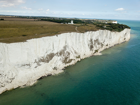 Aerial view of The White Cliffs of Dover.\nThe White Cliffs of Dover is the region of English coastline facing the Strait of Dover and France. The cliff face, which reaches a height of 350 feet (110 m), owes its striking appearance to its composition of chalk accented by streaks of black flint, deposited during the Late Cretaceous. The cliffs, on both sides of the town of Dover in Kent, stretch for eight miles (13 km). The White Cliffs of Dover form part of the North Downs. A section of coastline encompassing the cliffs was purchased by the National Trust in 2016.