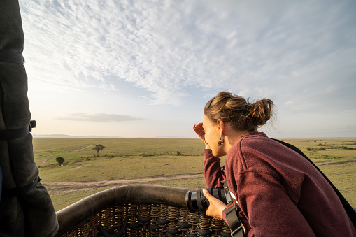 Woman peers over the edge of the basket while on a hot air balloon safari, in the Masaai Mara Reserve in Kenya