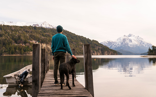 Boy with his best companion, a large dog, watch the sunset from a pier in Patagonia.