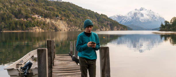 istock Young Man Controls His Cell Phone While Enjoying the Landscape on a Dock on Lake Bariloche. 1493261414