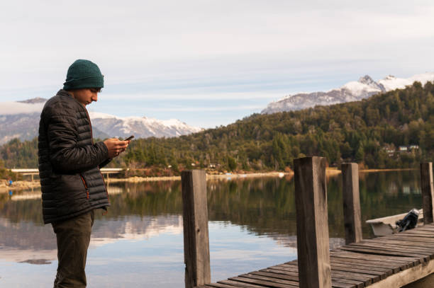 istock Young Man Controls His Cell Phone While Enjoying the Landscape on a Dock on Lake Bariloche. 1493261435