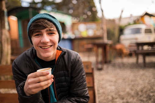 Smiling young man enjoying a coffee at a food truck during his winter vacation in Patagonia.