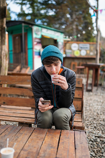 A young man checks his text messages on his cell phone while having a coffee sitting in a food truck space in Patagonia during his visit.
