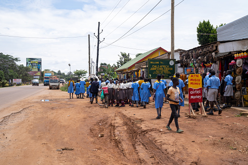 Kayabwe, Uganda - March 21, 2023: School children in uniform walk near a market in the tourist area of the Equator line
