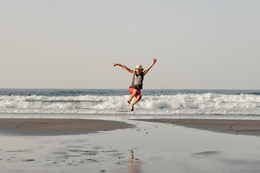 Happy teenage girl with straw hat jumping on the seashore on a beach in Tenerife, travel concept